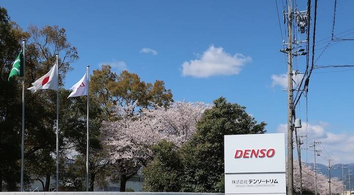 満開の桜と青空を背景にした株式会社デンソートリムの看板と工場外観。
