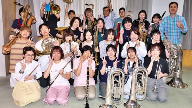 四日市吹奏楽団の団員たちが楽器を手に、第45回定期演奏会へ向け笑顔を見せる様子