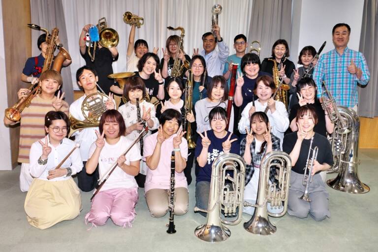 四日市吹奏楽団の団員たちが楽器を手に、第45回定期演奏会へ向け笑顔を見せる様子