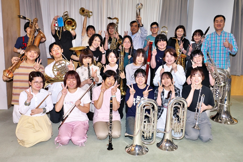 四日市吹奏楽団の団員たちが楽器を手に、第45回定期演奏会へ向け笑顔を見せる様子