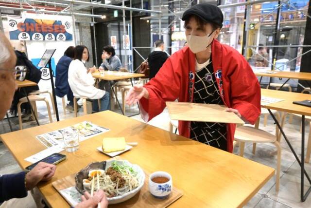赤い法被を着た女性が四日市まぜ麺を提供している
