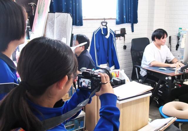 一眼レフカメラを使って社長を撮影する中学生