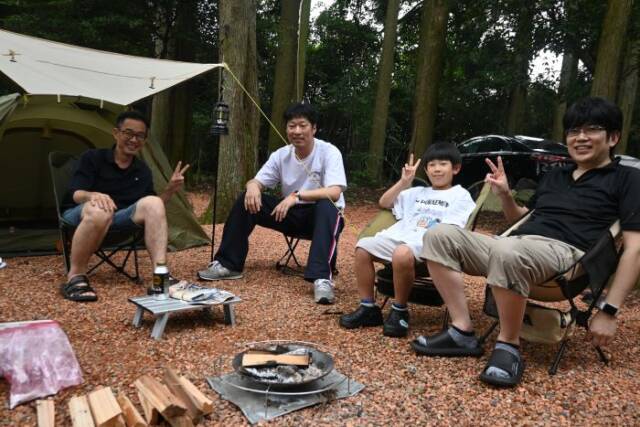 椅子に座りVサインをしてキャンプを楽しむ男性3人と子ども