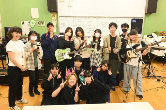 バンド部員の集合写真前列4人がピースサインをし、後列は楽器やマイクを手にしている