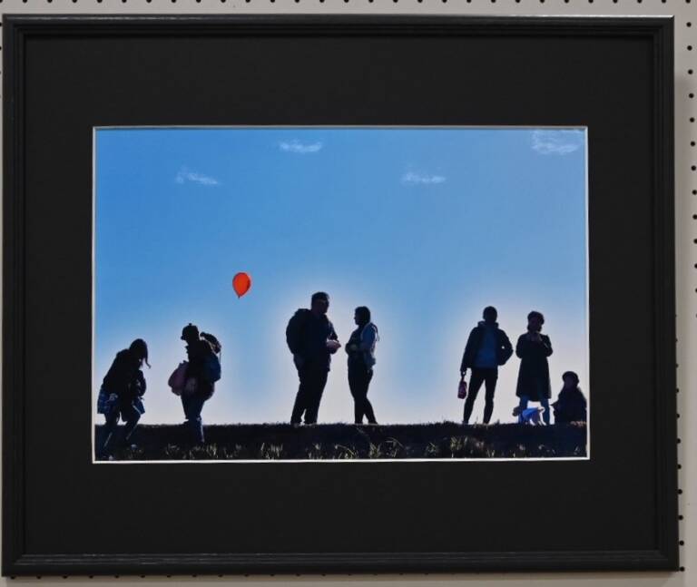 青空を背景に7人の人が立つ赤い風船が印象的な写真