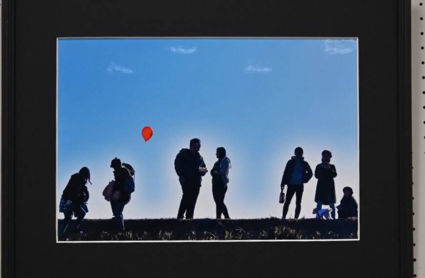 青空を背景に7人の人が立つ赤い風船が印象的な写真