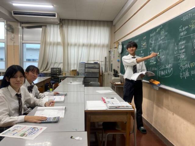 黒板を使い説明する男子生徒と説明を聞く女子生徒2人