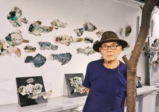 ギャラリーの白壁いっぱいに展示した陶の魚の前に立つ陶芸家の森正さん