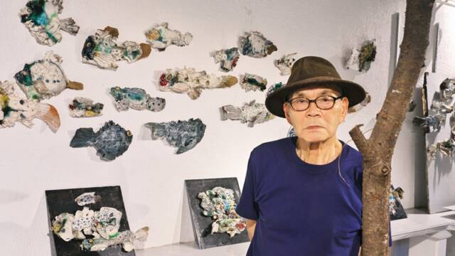 ギャラリーの白壁いっぱいに展示した陶の魚の前に立つ陶芸家の森正さん