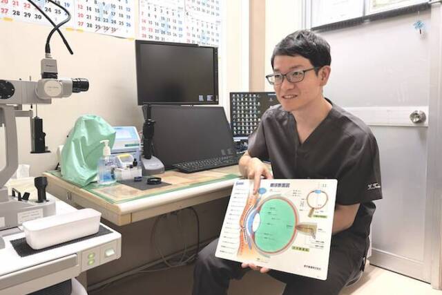 三重県立総合医療センター眼科の田中医師が、眼球の構造図を持ちインタビューに答えているいる。