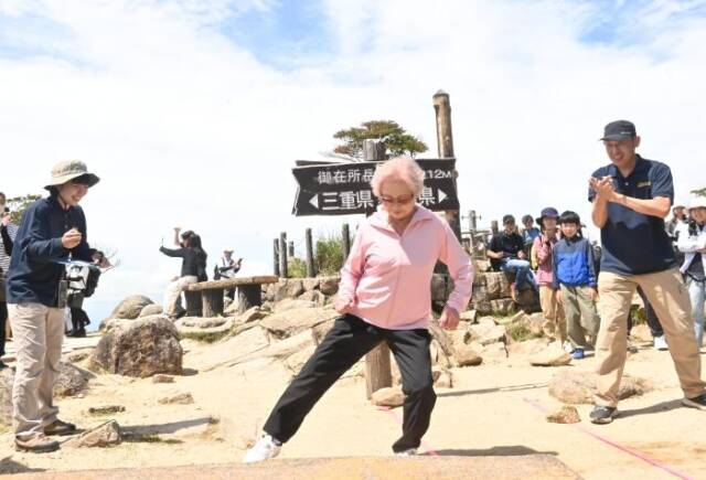 山頂の県境で反復横跳びに挑戦する90歳の女性