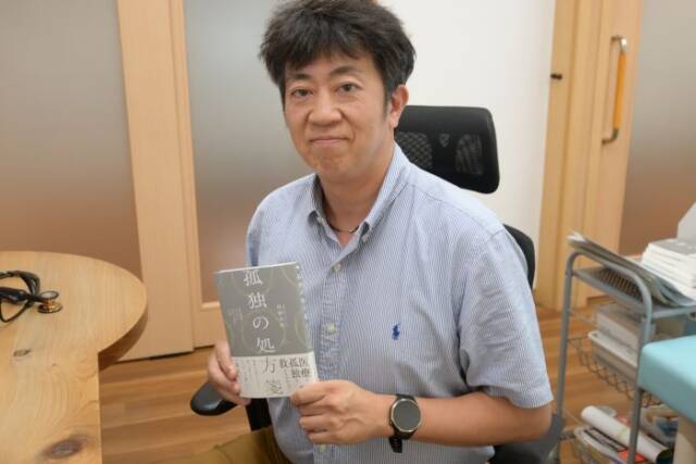 診察室で著書「孤独の処方箋」を手にする貝沼院長