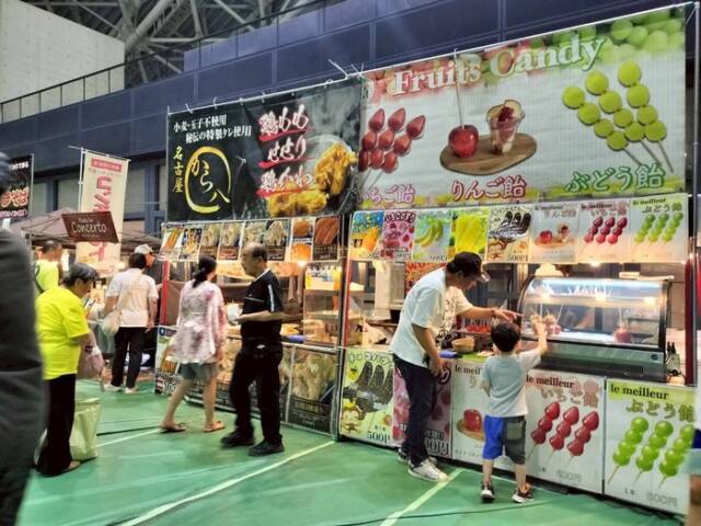 祭りの飲食店ブース前で、来場者がりんご飴や唐揚げを注文し受け取っている