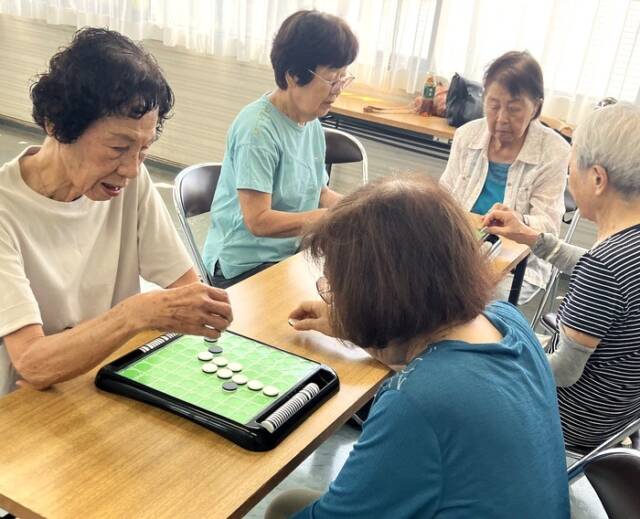 市民センター内のオセロコーナーで、女性たちが盤を囲んで対戦している光景。