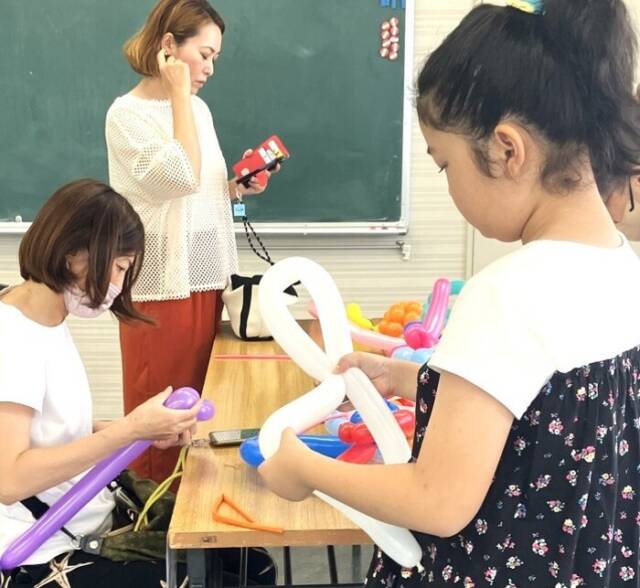 バルーンアートコーナーで、女の子が大人の女性と一緒に風船を触りながら作品づくりをしている様子。