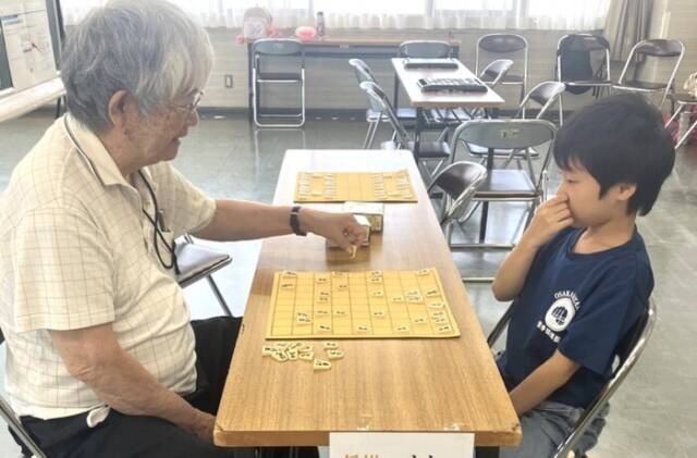 将棋盤を前に、年配の男性と小学校低学年くらいの男の子が集中して対局している場面。