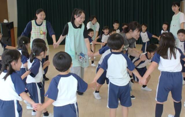 子どもたちと手をつなぎ、音楽に合わせて運動する高校生ら