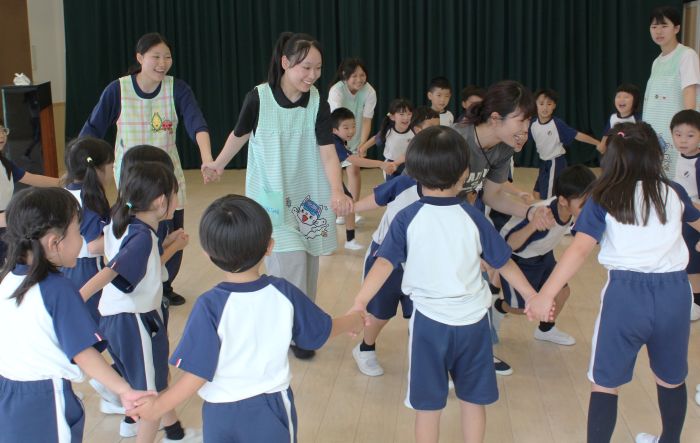 子どもたちと手をつなぎ、音楽に合わせて運動する高校生ら