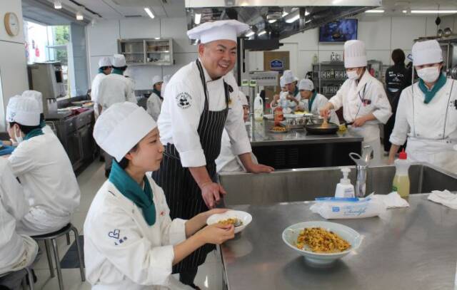 調理した炒飯を試食する学生たちと白川貴久シェフ