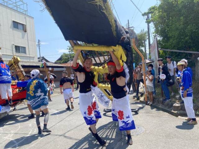 鯨を担ぐ祭りの2人の担い手とそれを見守る人