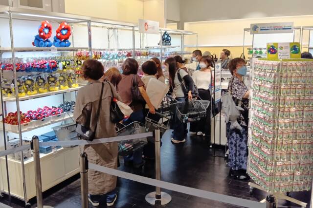 公式グッズが並ぶ売り場で商品を選ぶ来店客