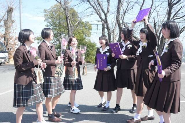 卒業式で旧制服を着た卒業証書を手にする3年生と花束を持つ現在の制服を着た2年生