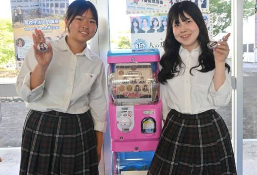 ガチャの横でキーホルダーを手にする2人の生徒