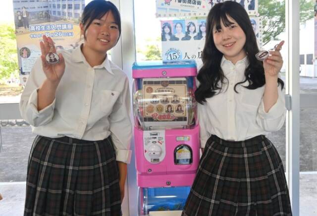 ガチャの横でキーホルダーを手にする2人の生徒