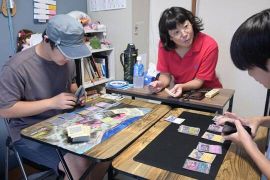ポケモンカードで遊ぶ子どもに話しかける生川さん(中央)